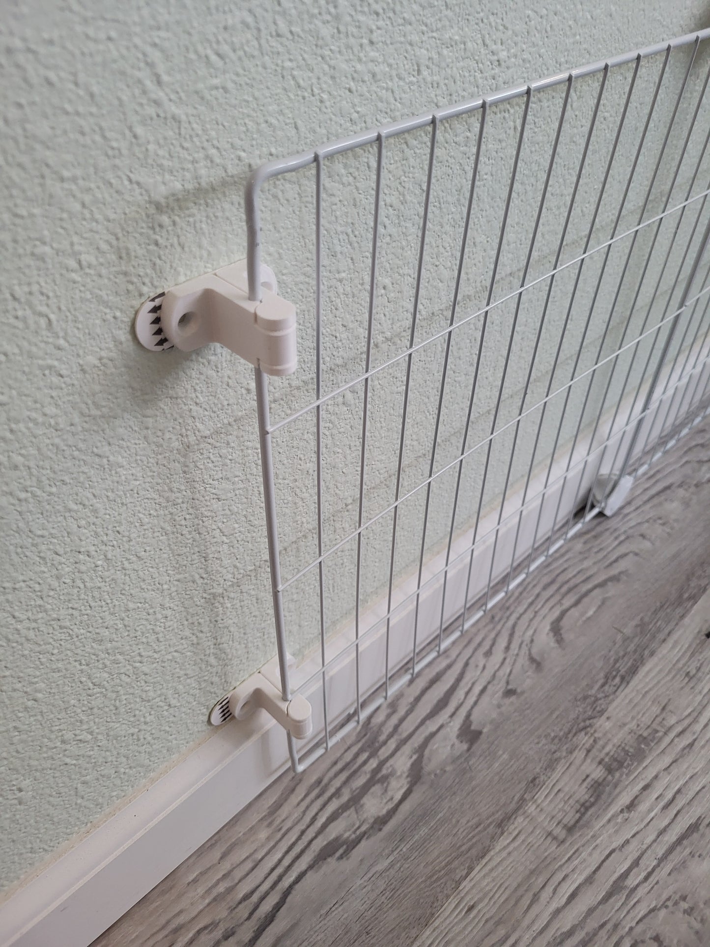 Pet xpen panels attached temporarily to the wall with adhesive strips to prevent rabbits from chewing baseboards