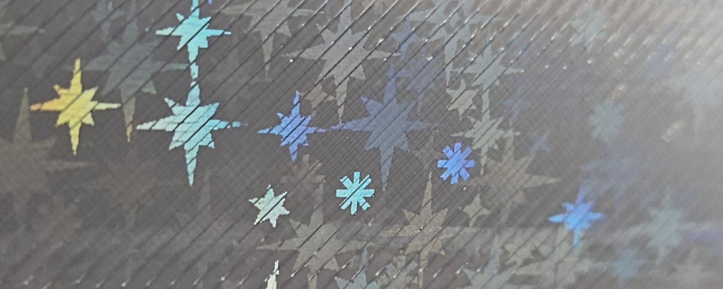 A close-up of a dark textured surface with scattered iridescent star and snowflake-like decals in blue, purple, yellow, and gray tones.