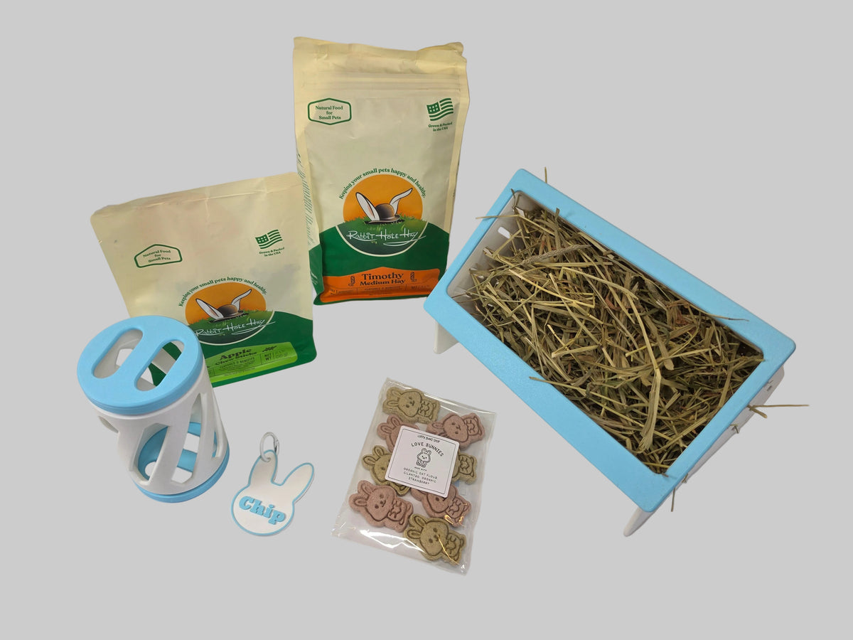 a bundle for rabbits including a bag of hay, a bag of apple chew sticks, a hay roller, a name tag, a bag of treats and a blue and white hay feeder