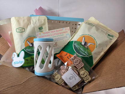 a bundle for rabbits including a bag of hay, a bag of apple chew sticks, a hay roller, a name tag, a bag of treats and a blue and white hay feeder just unpacked